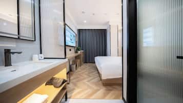 Una habitación de hotel moderna con una cama grande, un baño con lavamanos y espejo, y una televisión.