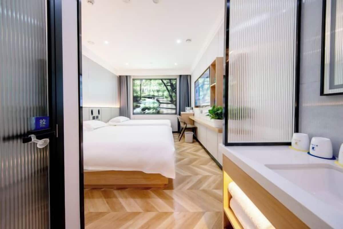 A modern hotel room with a large bed, a desk, a mirror, and a view of greenery.