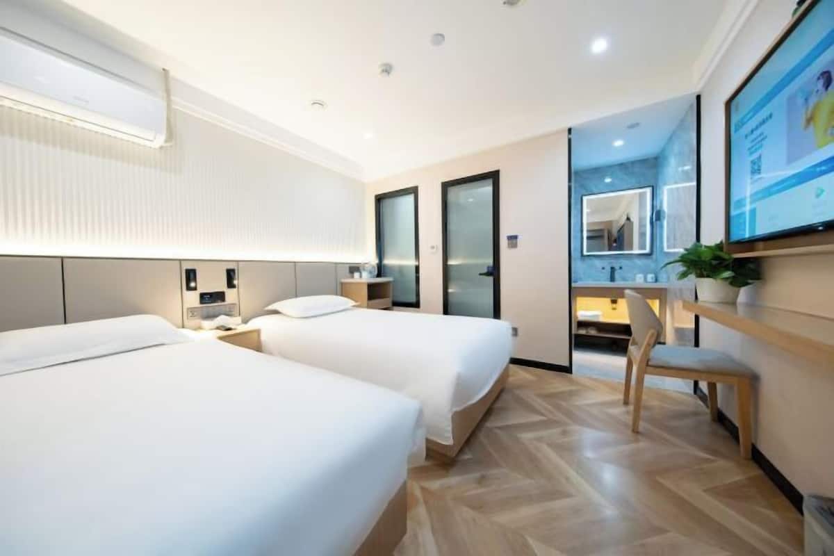 A hotel room with two beds, a desk, a chair, a mirror, and a television.