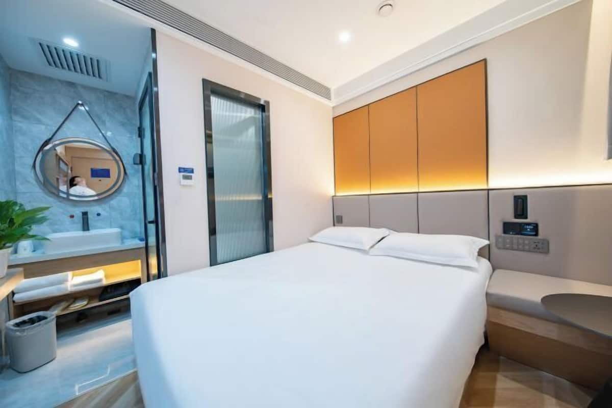 A modern hotel room with a bed, a bathroom with a mirror, and a bedside table.