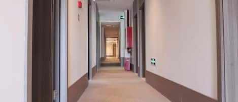 A hotel corridor with doors on both sides, a carpeted floor, and a visible exit sign.