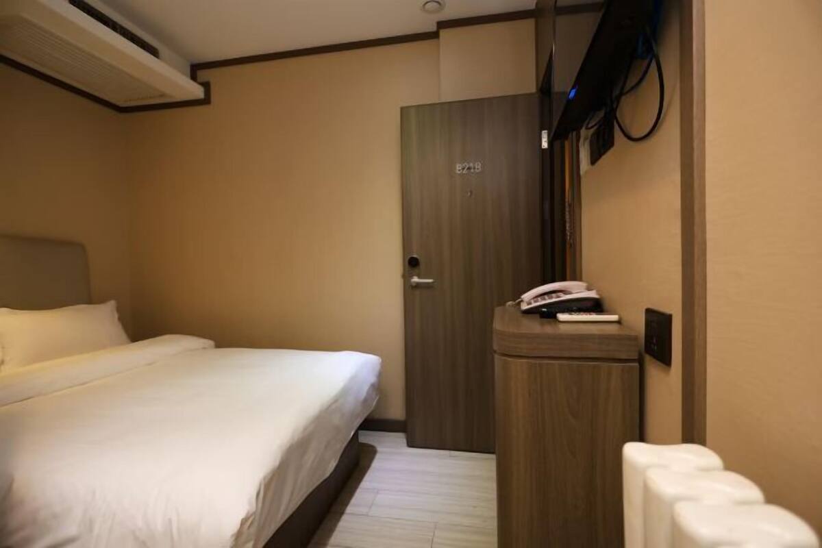Habitación de hotel con cama, puerta de madera, escritorio con teléfono y televisor montado en la pared.