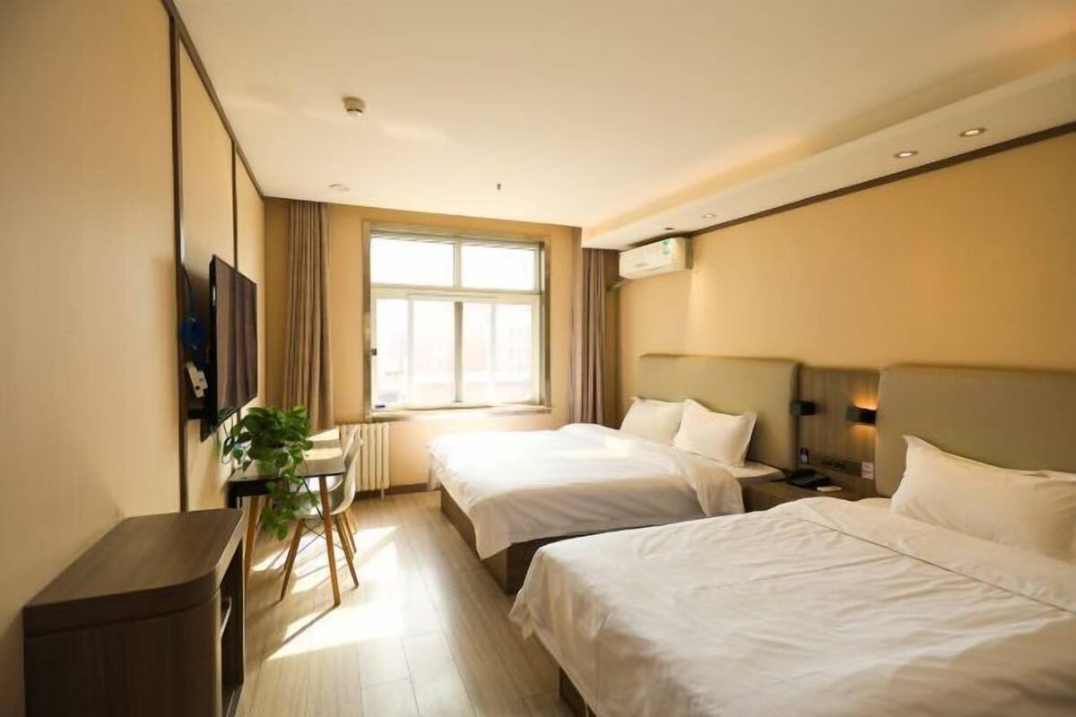 Habitación de hotel con dos camas, un escritorio, una silla, una planta y una ventana con cortinas.