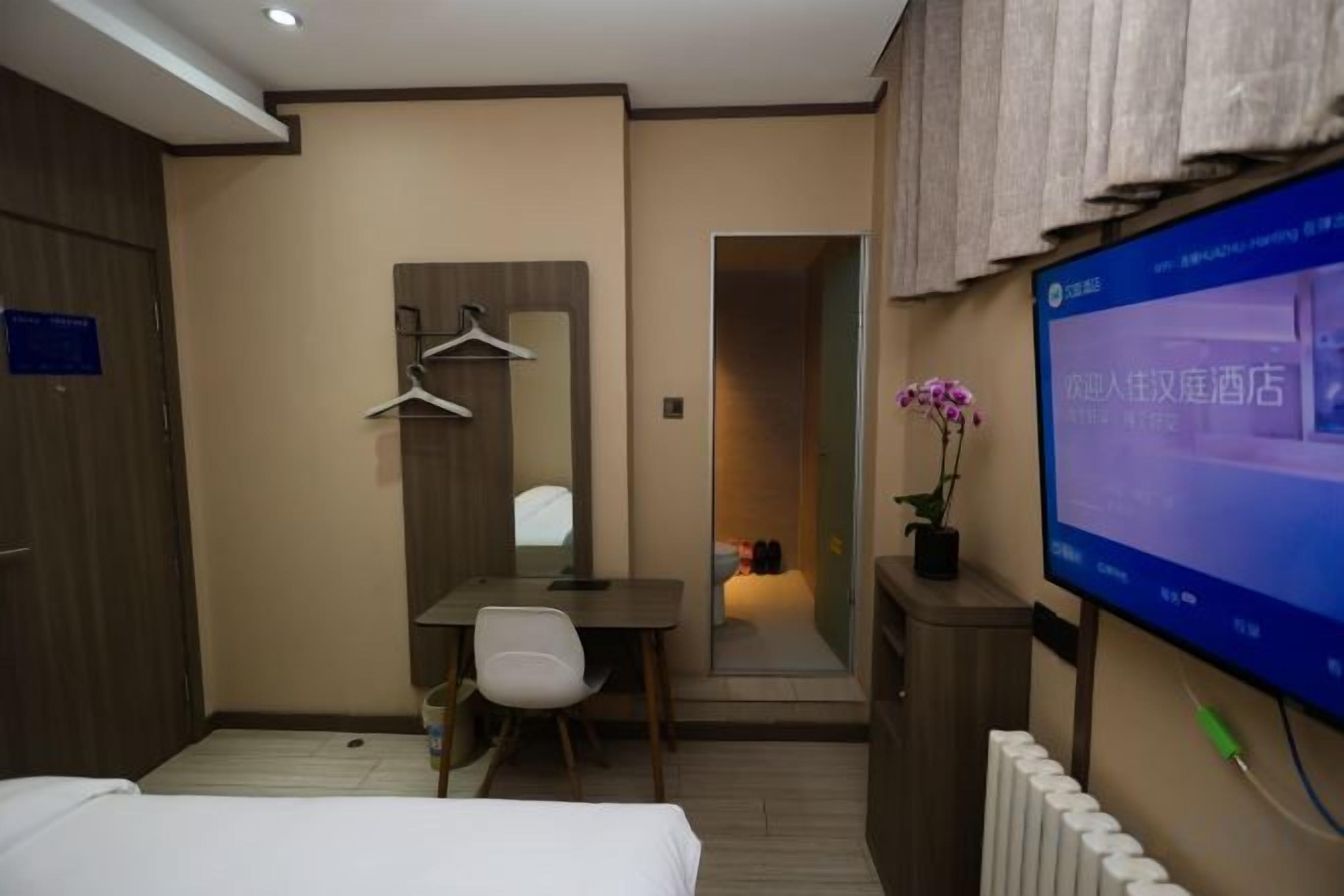 A hotel room with a bed, a desk, a chair, a television, and a mirror.