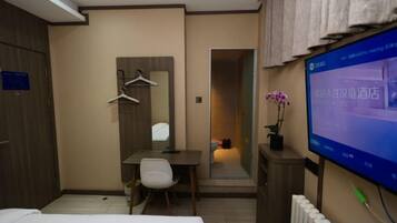 A hotel room with a bed, a desk, a chair, a television, and a mirror.