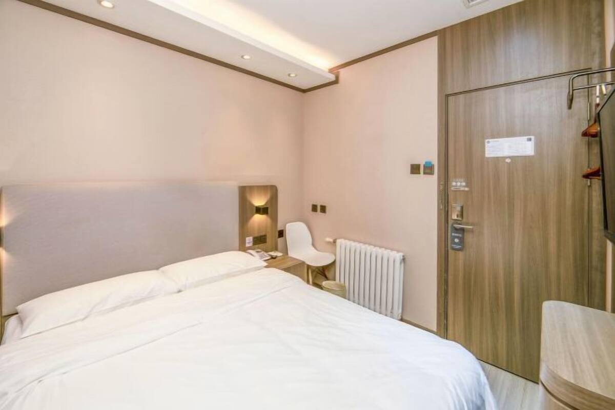 Una habitación de hotel con una cama, una silla, un escritorio, un radiador y una puerta de madera.