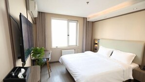 Et hotelværelse med en seng, fjernsyn, skrivebord, stol, radiator og et vindue.