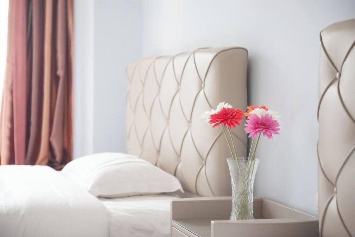 A hotel room with a bed, a nightstand with a vase of flowers, and a headboard.
