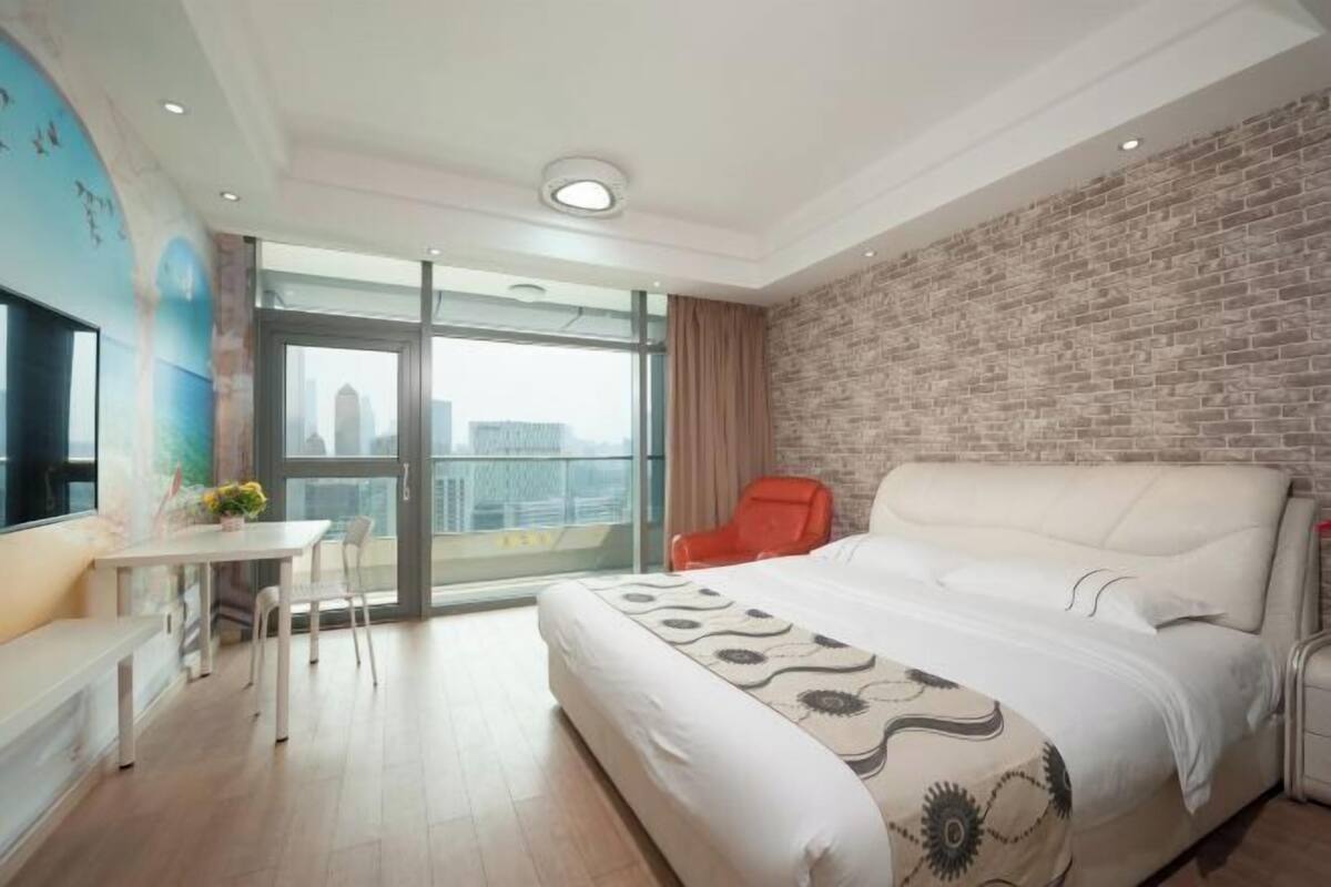A modern hotel room with a large bed, a desk, a chair, and a balcony with a city view.