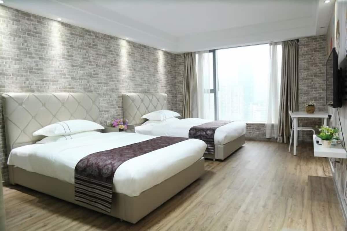 A hotel room with two beds, a small desk, and a large window with curtains.