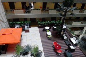 A multi-level indoor space with seating areas, a palm tree, and a view of the lower level.