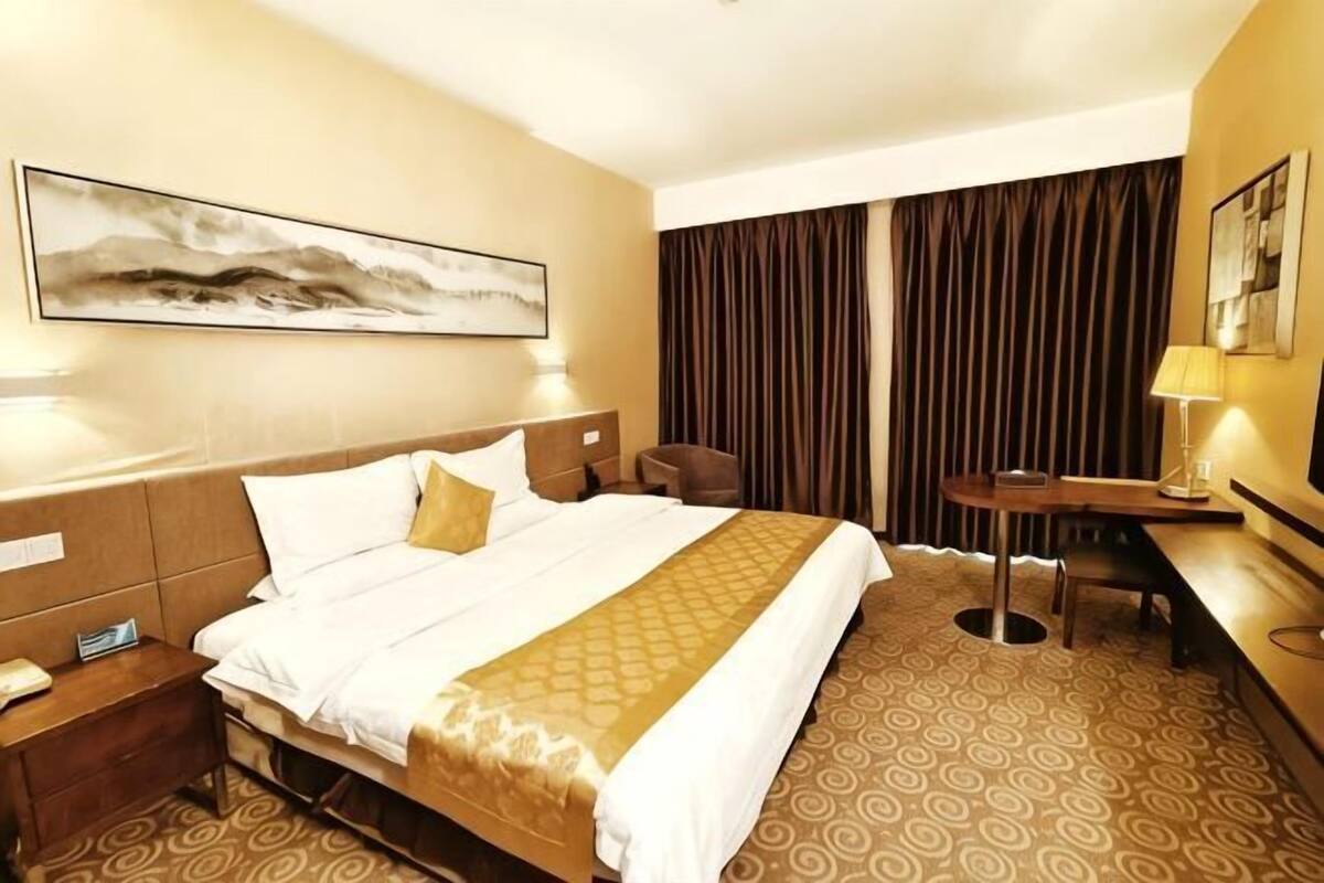 A hotel room with a bed, a desk, a chair, a lamp, and a painting on the wall.