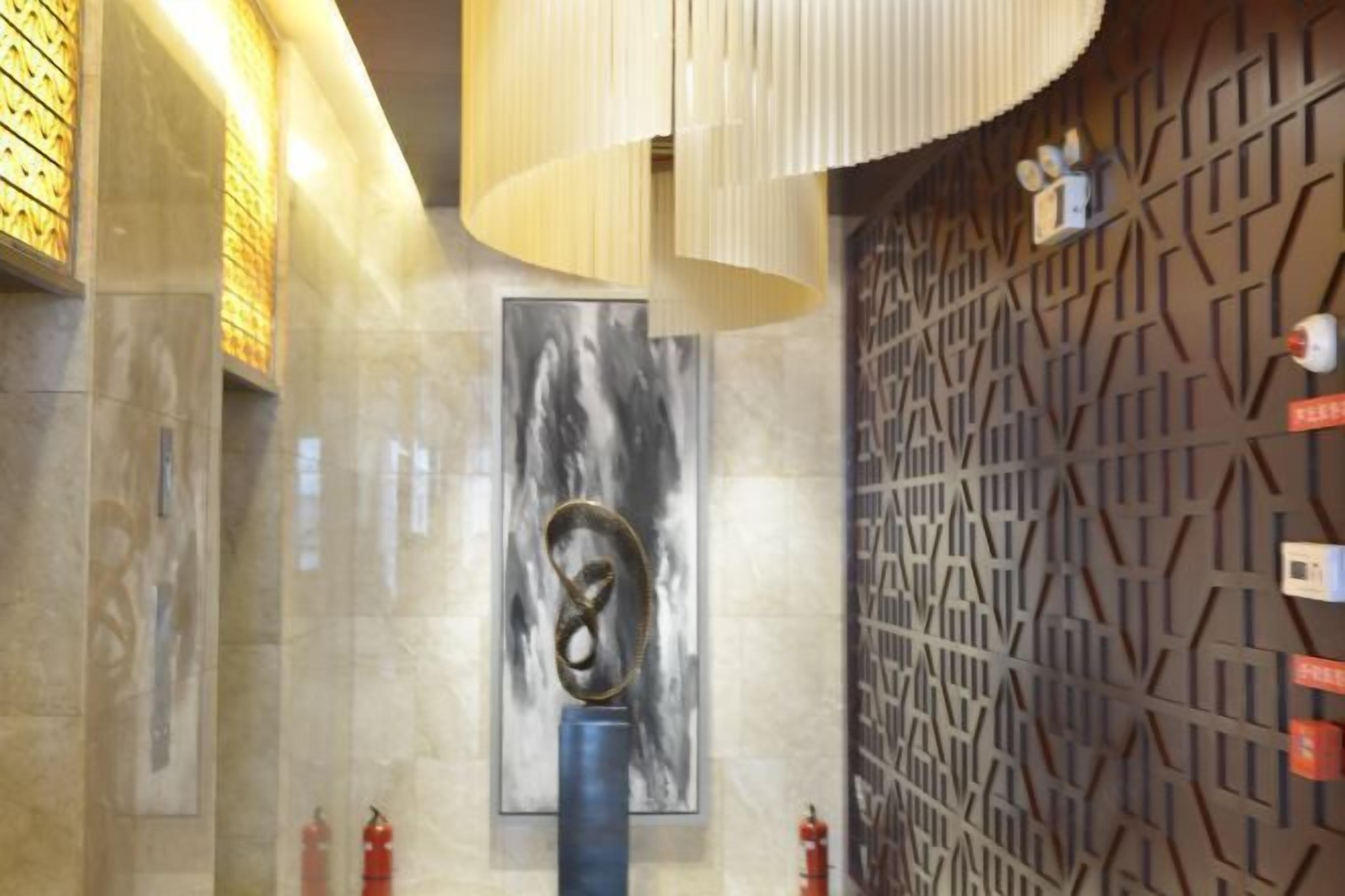 En modern entréhall med ett marmorgolv, en stor, abstrakt skulptur och en vägg med ett mönster.