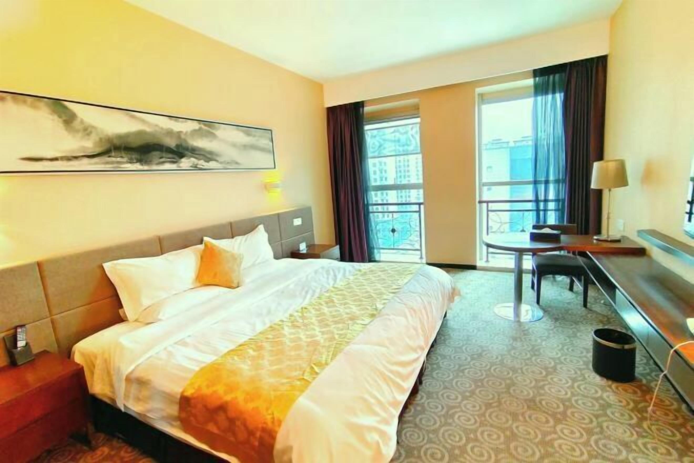 Quarto de hotel com cama, escrivaninha, cadeira, janela e um quadro na parede.