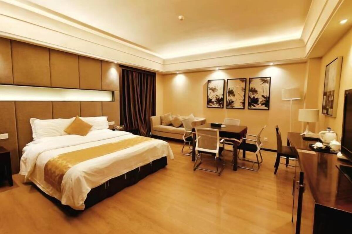 A hotel room with a bed, a desk, a chair, a sofa, and artwork on the walls.