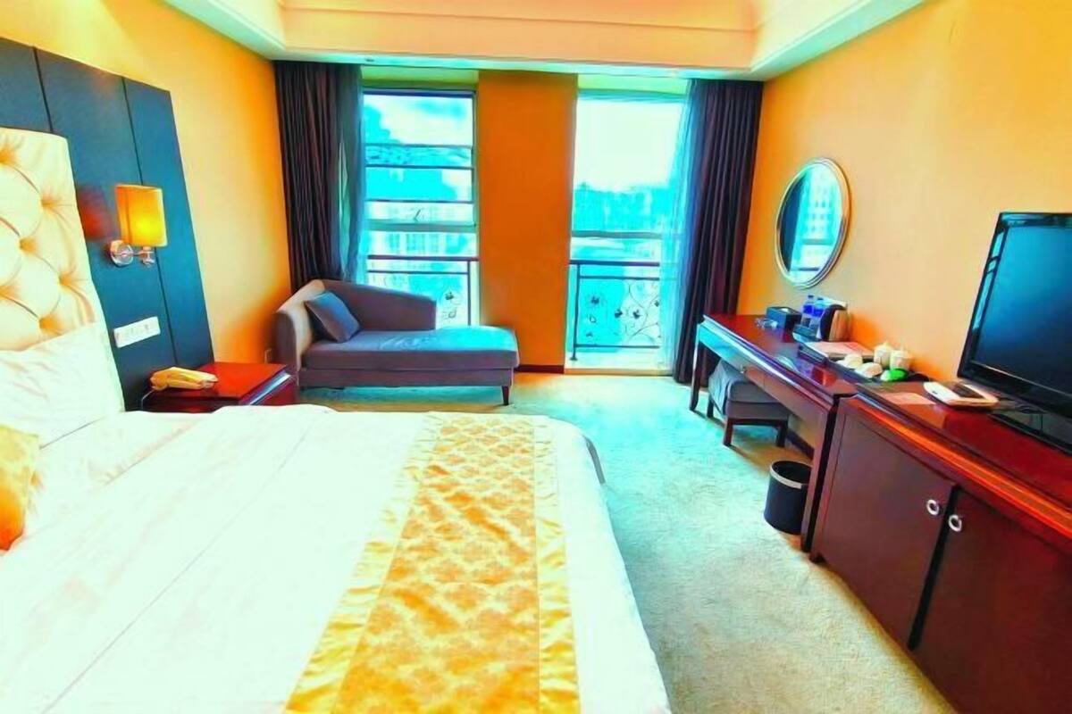 A hotel room with a bed, a desk, a chair, a television, and a view of the outside.