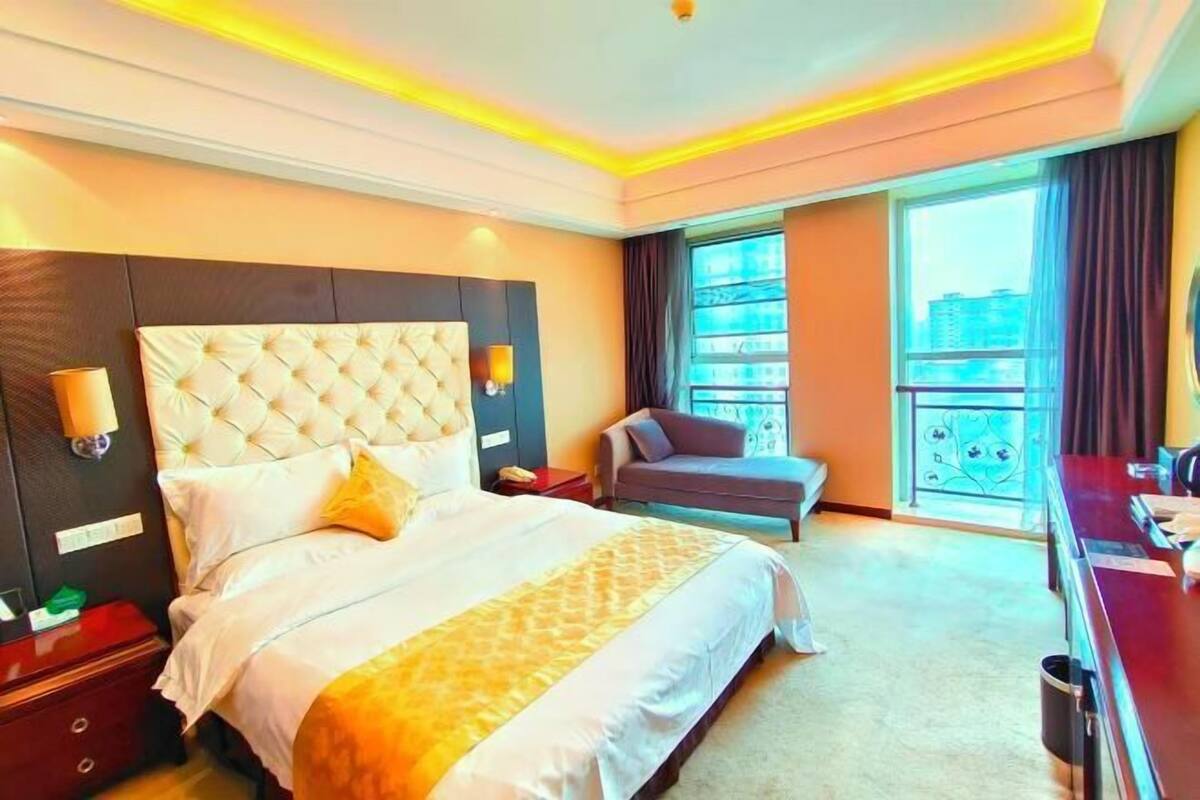 A hotel room with a large bed, a desk, a chair, and a balcony with a view.