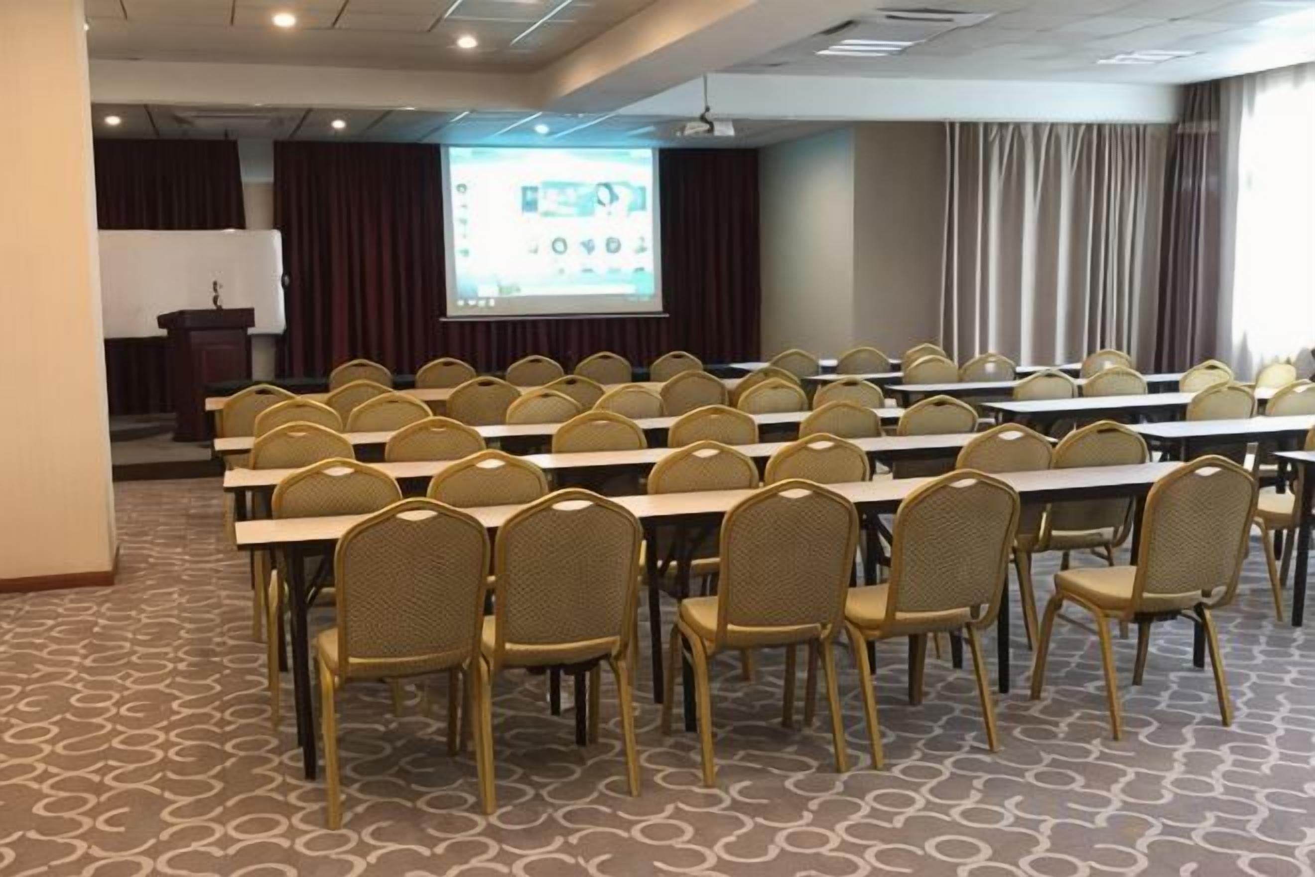 A conference room with rows of tables and chairs, a podium, and a projection screen.