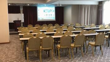 A conference room with rows of tables and chairs, a podium, and a projection screen.