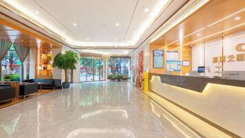 A hotel lobby with a reception desk, seating area, and a large plant.