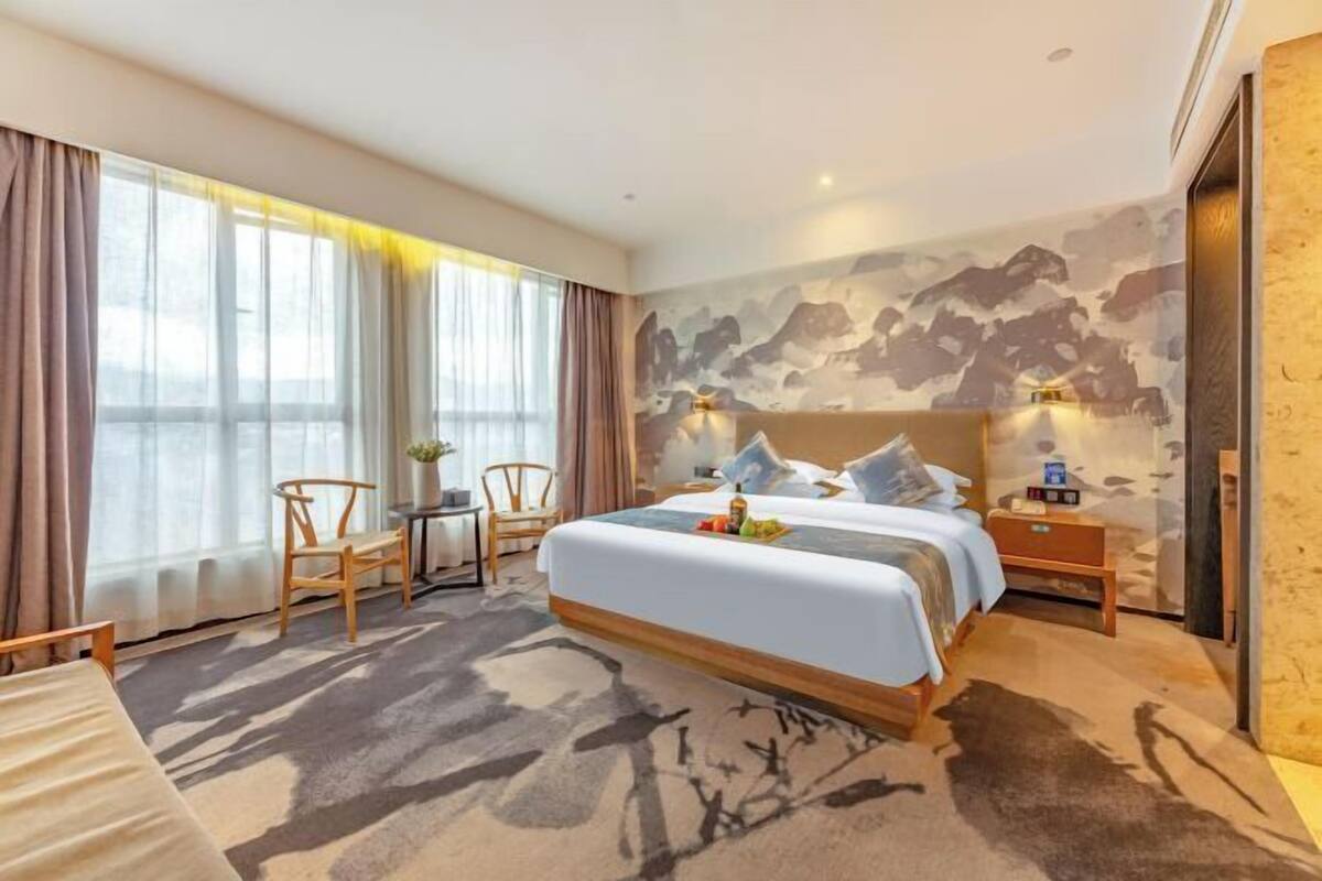 A hotel room with a bed, a desk, chairs, a small table, and a large window.