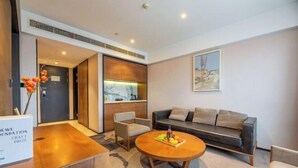 A modern living room with a sofa, coffee table, and chairs. There is a dining table with a vase of flowers. A painting is on the wall, and a door is visible in the background. - Sea Trek Star Exquisite Hotel (Lishui)
