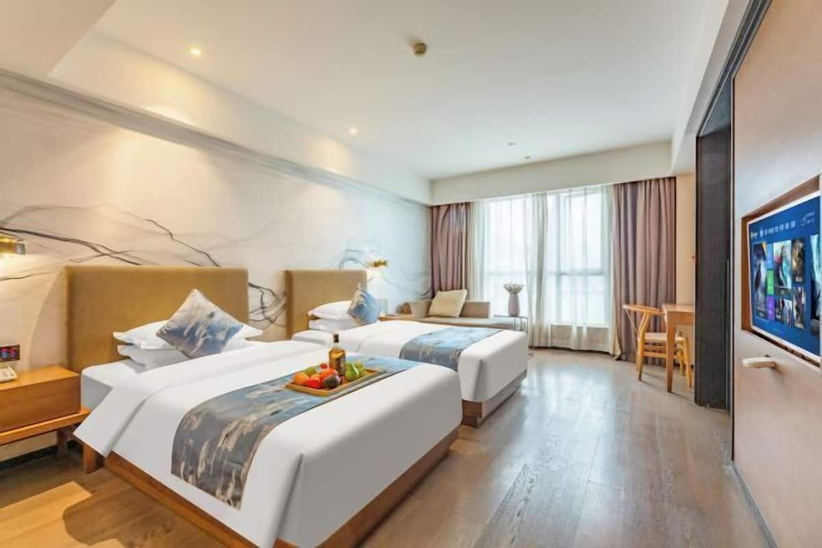 A hotel room with two beds, a desk, a chair, and a television.