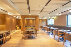 Un salón de conferencias con varias mesas y sillas, paredes de paneles de madera y ventanas amplias.