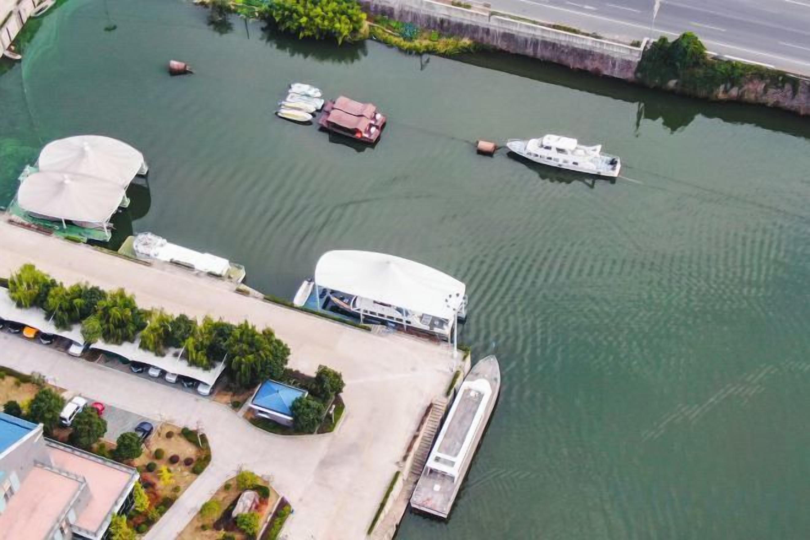 Une vue aérienne d’une marina avec des bateaux amarrés, un grand bâtiment blanc et un pont en arrière-plan.
