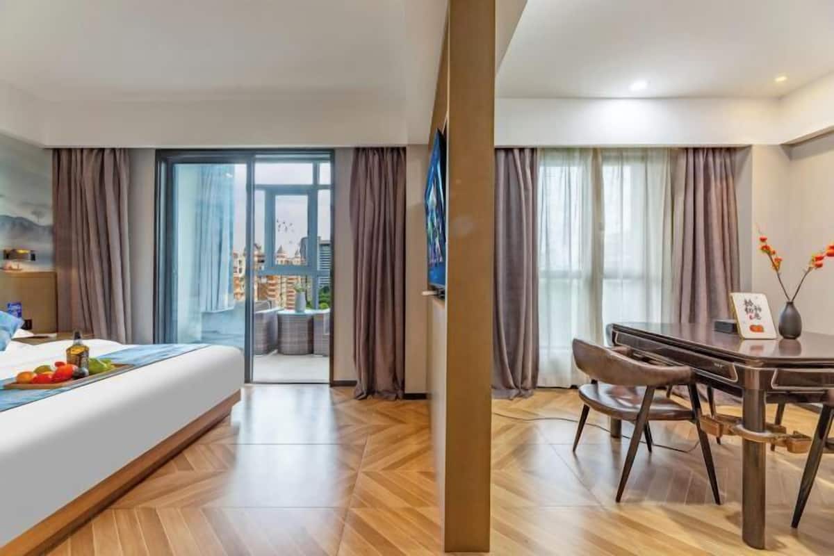 A hotel room with a bed, a dining table, and a view of the city.