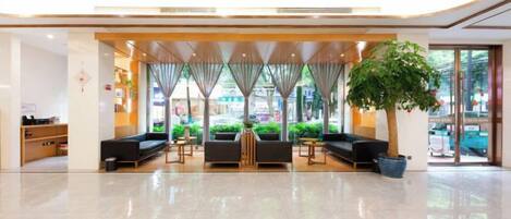 Un hall d’hôtel comprenant un comptoir d’accueil, un espace salon et une grande plante en pot.