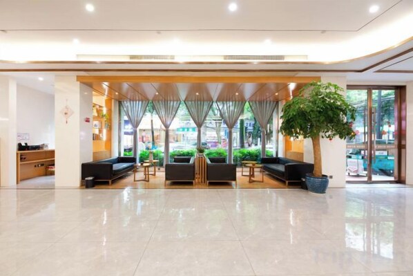 Un vestíbulo de hotel con mostrador de recepción, área de estar y una planta grande en maceta.