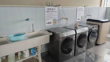 A public restroom with a sink, two washing machines, and a trash bin.