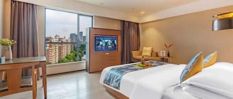 A hotel room with a bed, a desk, a TV, and a view of the city.