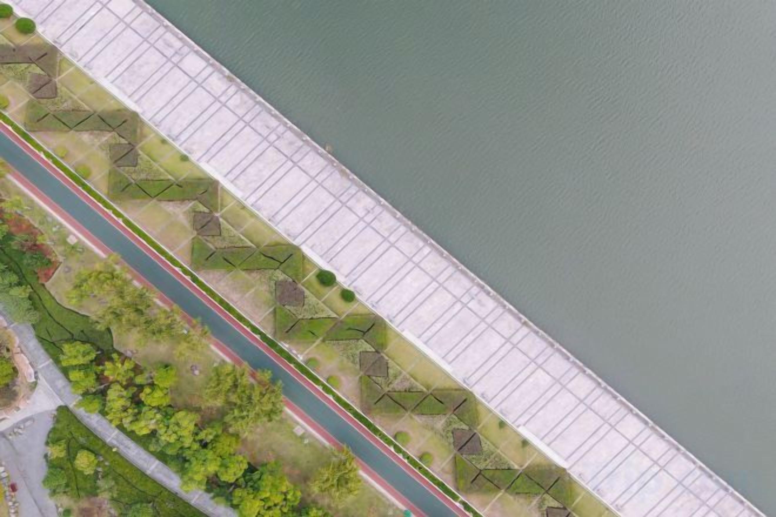 A bridge with a pathway and greenery on one side, and a water body on the other.
