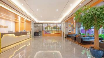 A hotel lobby with a reception desk, seating area, and a large potted plant.
