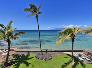 A tropical resort with palm trees, a clear blue ocean, and a view of a mountain in the distance.