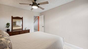 A bedroom with a bed, a ceiling fan, a dresser, a mirror, and a door leading to a staircase.