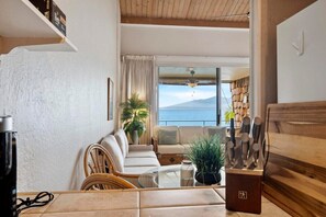A modern living room with a sofa, a glass coffee table, and a view of the sea.