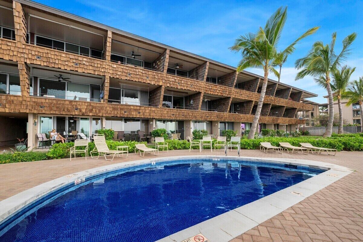 A hotel with a pool area, multiple balconies, and palm trees.