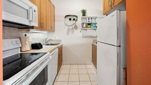 A compact kitchen with wooden cabinets, a white refrigerator, a microwave, an oven, and a sink. - Oceanfront Maui Condo-Walk to Beach, Shops, Cafés (Lahaina)