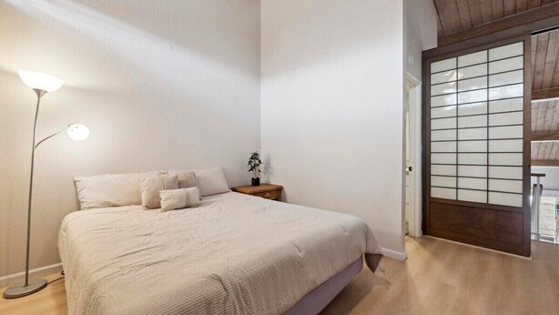 A bedroom with a bed, bedside lamp, nightstand, and a shoji screen door. - Oceanfront Maui Condo-Walk to Beach, Shops, Cafés (Lahaina)