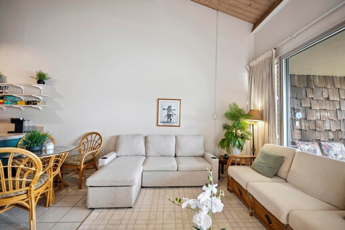 A modern living room with a sofa, a dining table with chairs, and a small side table with a lamp.