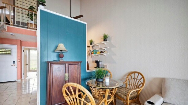 Un salon avec une table ronde en verre, des fauteuils en osier, un paravent bleu et un canapé blanc.