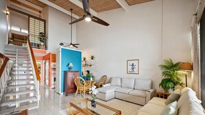 A spacious living area with a staircase, a blue accent wall, a sofa, and a coffee table. - Oceanfront Maui Condo-Walk to Beach, Shops, Cafés (Lahaina)