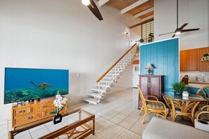 Amplia sala de estar con escalera de madera, una mesa de comedor con sillas y un televisor mostrando una escena submarina.