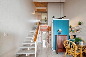 Eine Treppe führt zu einer Zwischenebene mit einer blauen Trennwand, einem Essbereich mit Korbstühlen und einem kleinen Tisch mit einer Lampe.