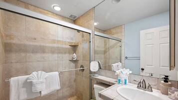 Een moderne badkamer met een glazen douchecabine, een grote spiegel, een wastafel met bijpassend meubilair en een handdoekrek.