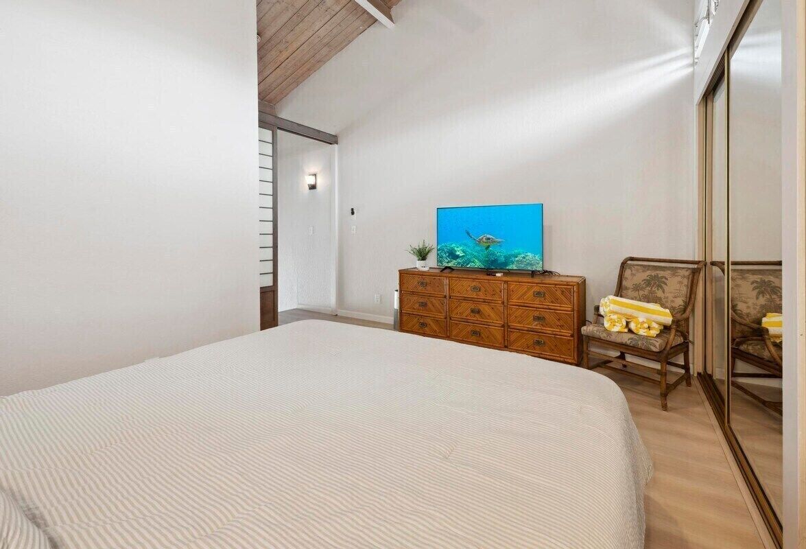 A bedroom with a large bed, a wooden dresser, a chair, and a painting on the wall.