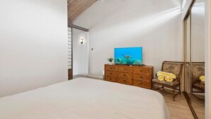 Une chambre à coucher avec un grand lit, une commode en bois, une chaise et un tableau accroché au mur.